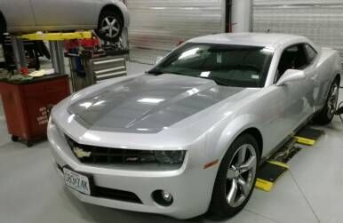 Silver Chevrolet Camaro in a garage, hood with grey accent, on a lift. | St. Louis Auto & Truck Repair
