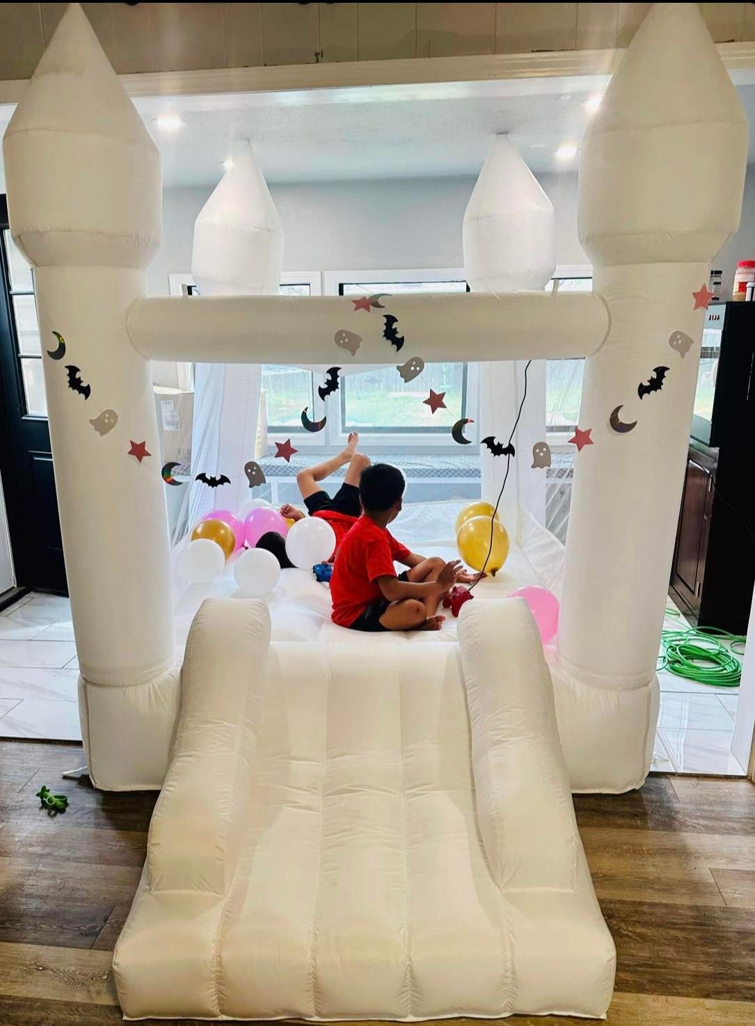 Two children playing in a white inflatable bounce house with a slide, decorated for a party.