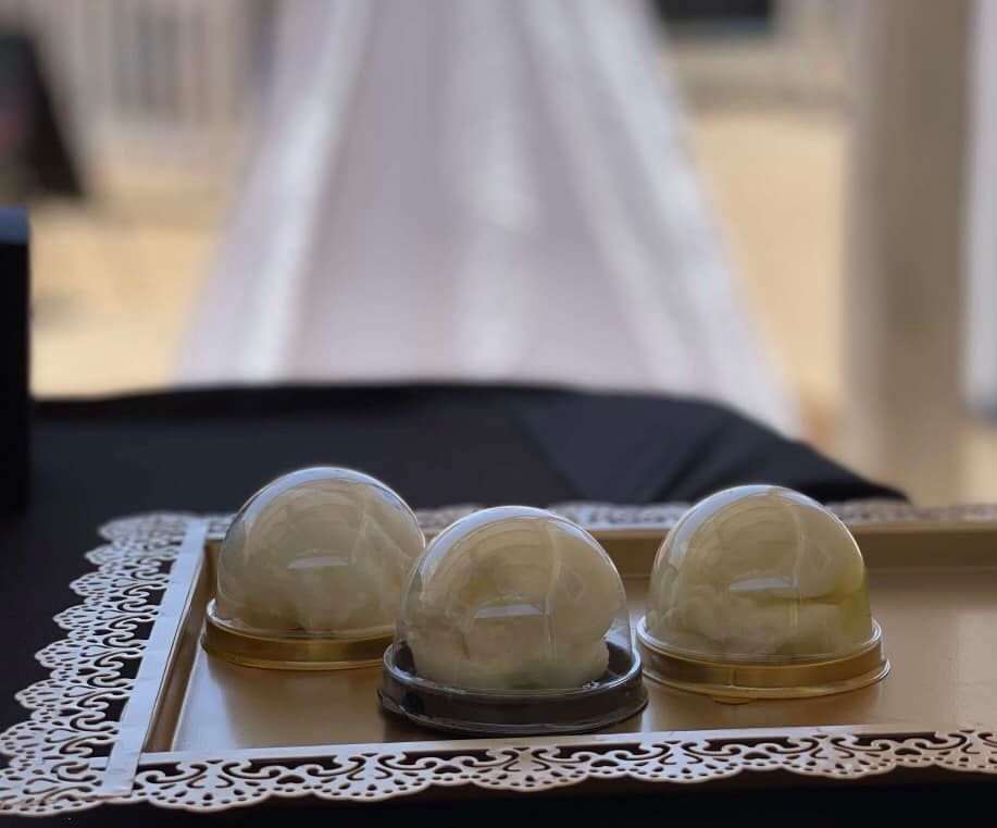 Three white, dome-shaped desserts on a gold tray with decorative edges, against a blurred white backdrop.