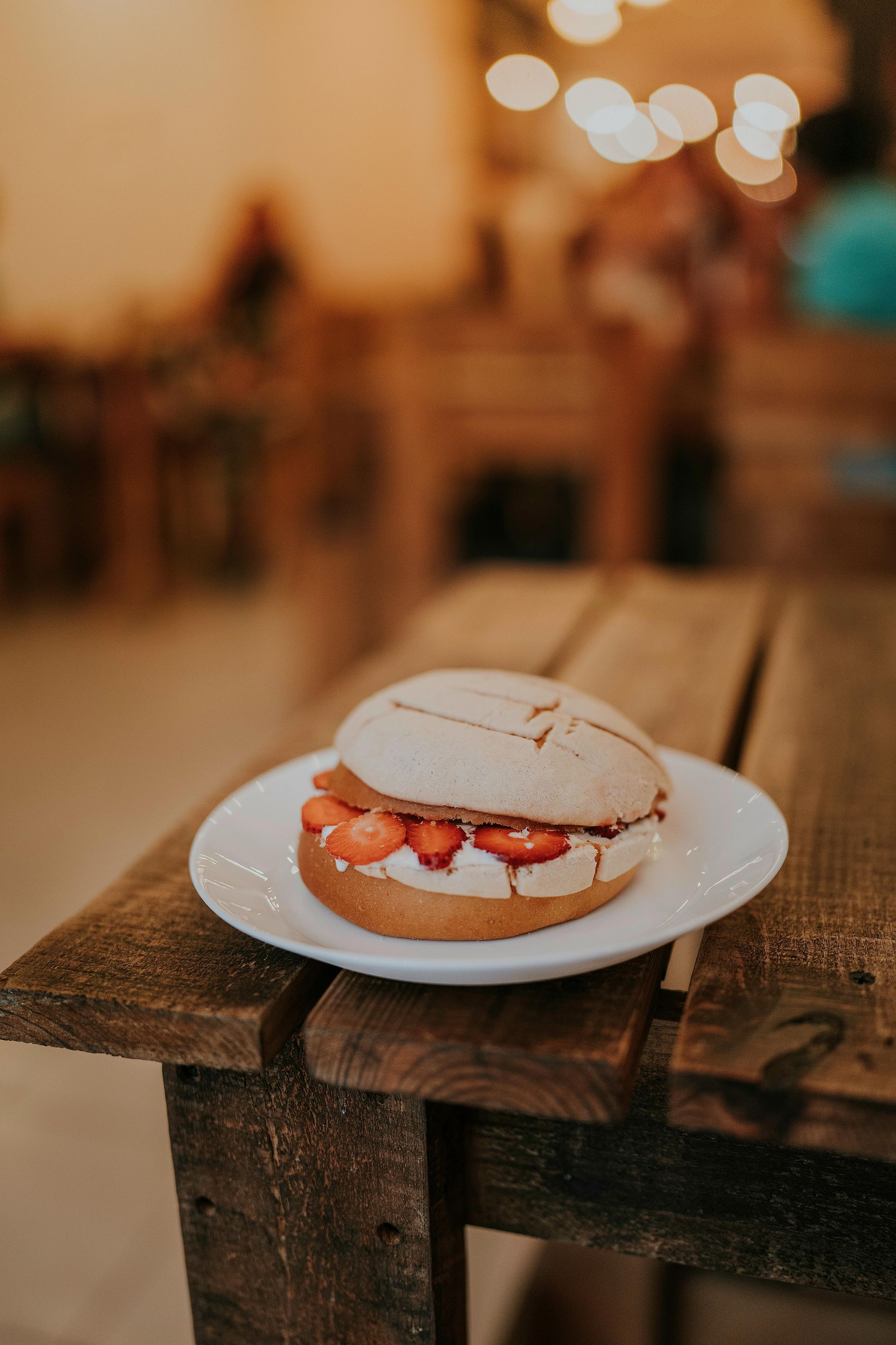 Strawberry dessert sandwich on a white plate, resting on a wooden table in a warm-lit cafe.
