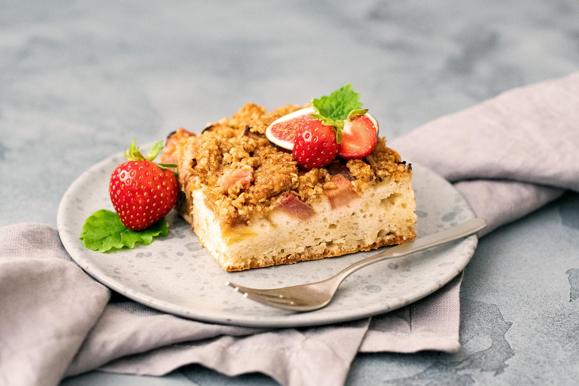 Strawberry rhubarb crumble cake on a plate with strawberries and a fork.