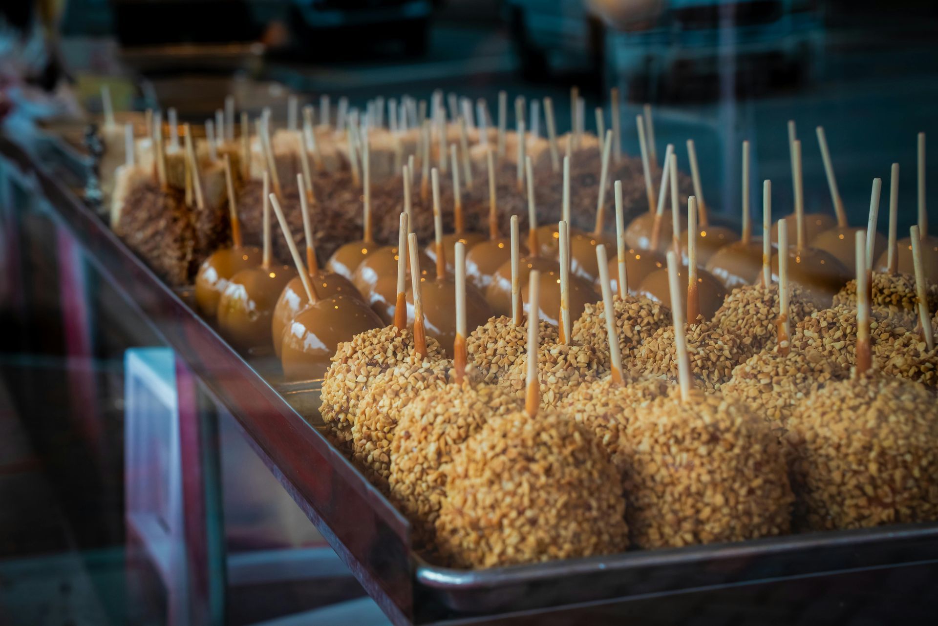 Caramel and nut-covered apples on sticks in a display case at a sweet shop.