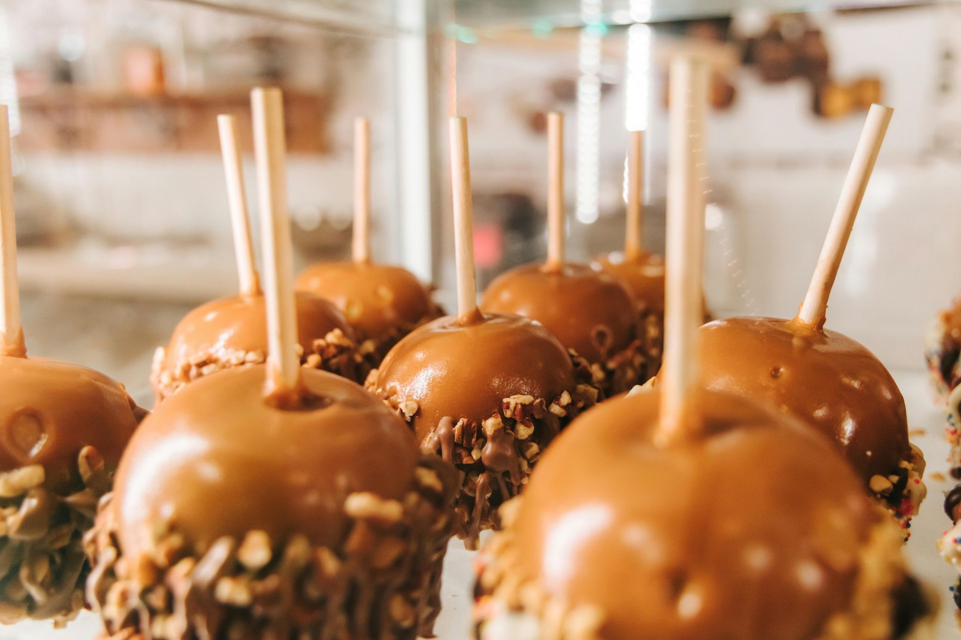 Caramel apples on display. Brown caramel coating with nuts, wooden sticks, inside a glass case.
