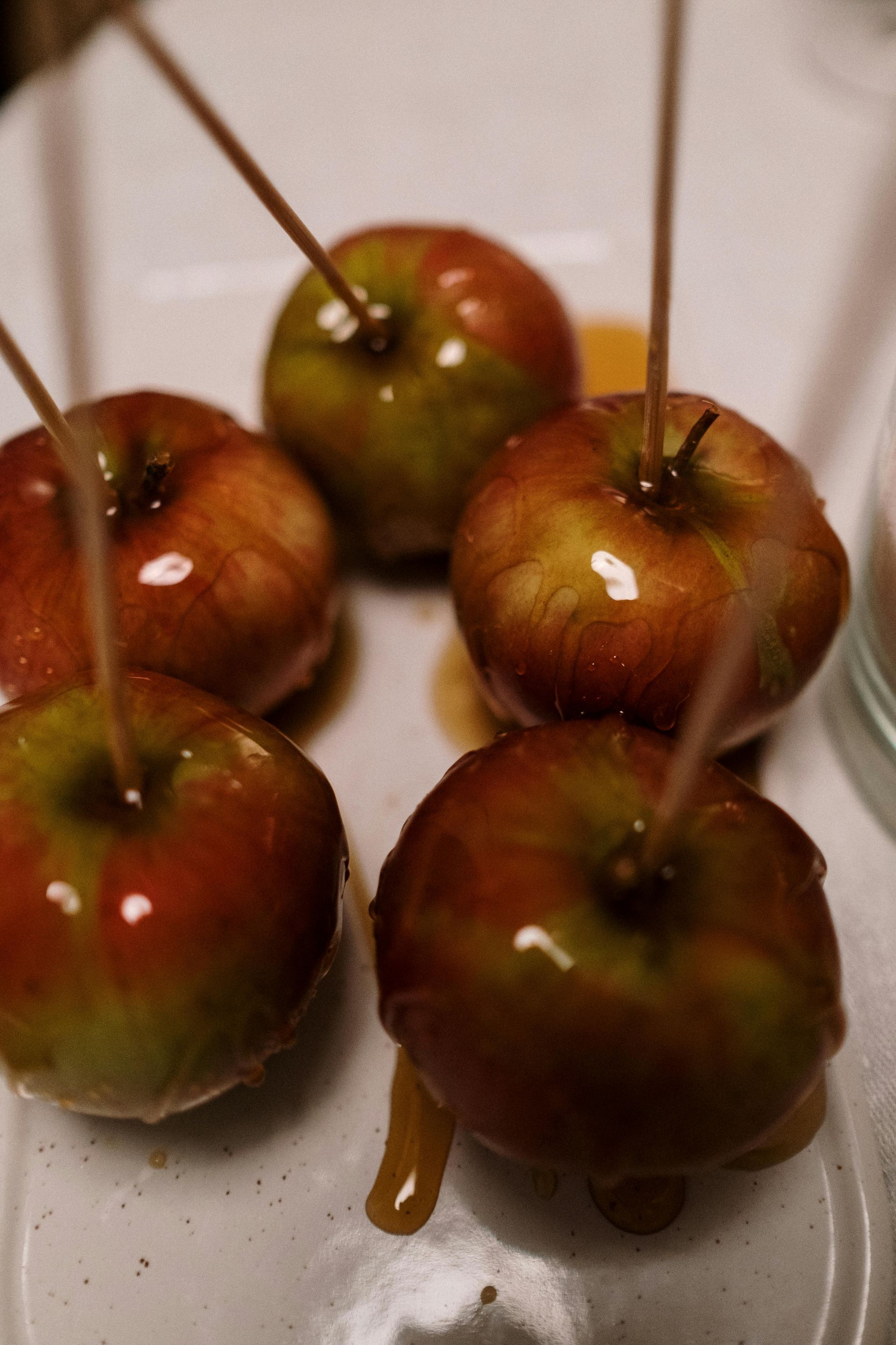 Caramel apples on a white plate with wooden sticks inserted. Caramel drips down the sides.