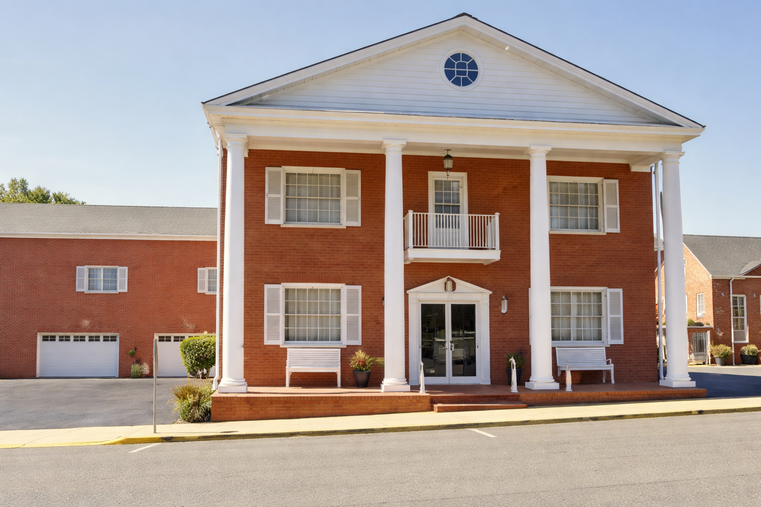 Red brick building with white columns and shutters, entrance with double doors, benches.