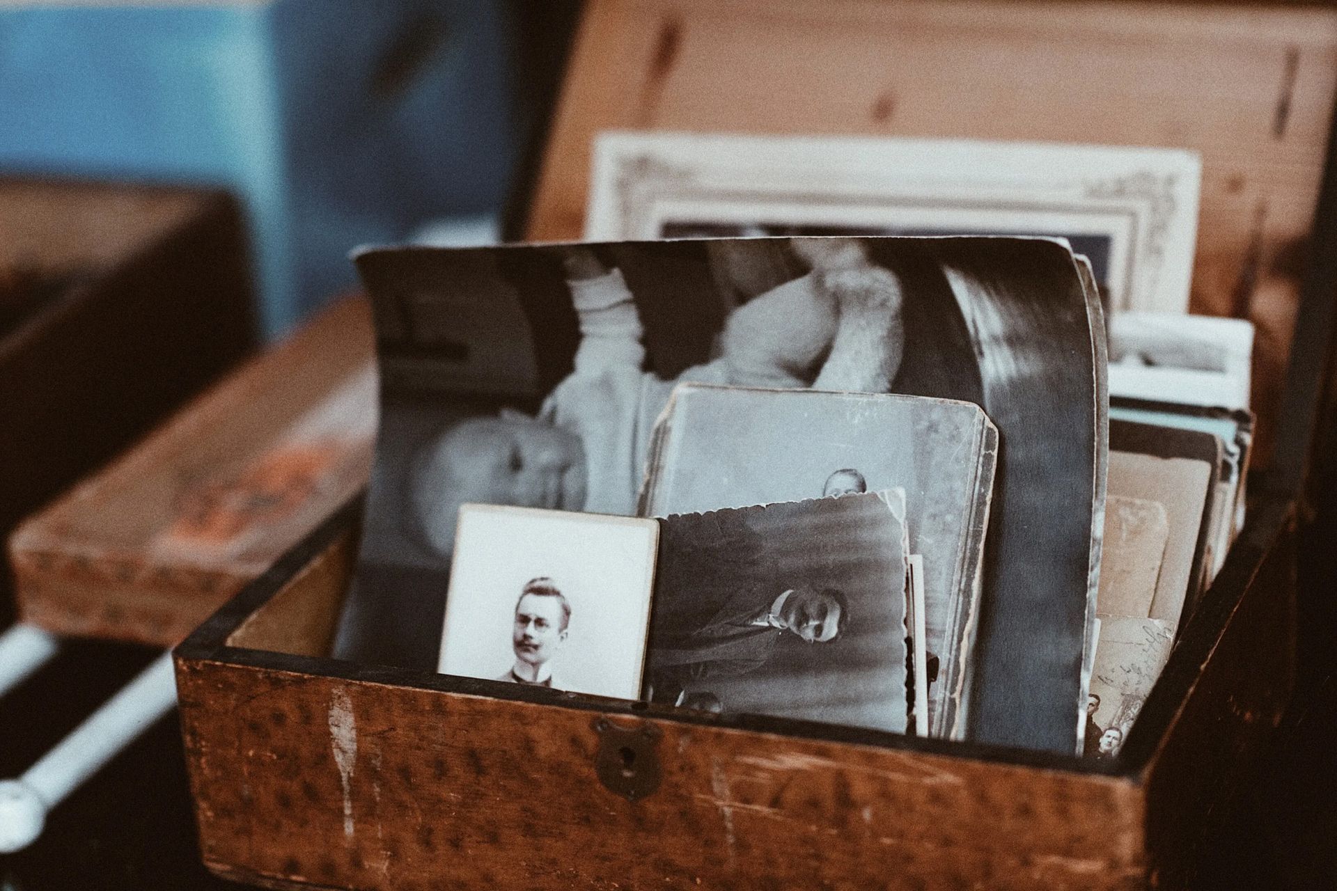 Wooden box filled with old photographs; baby, man, and assorted images, sepia-toned.
