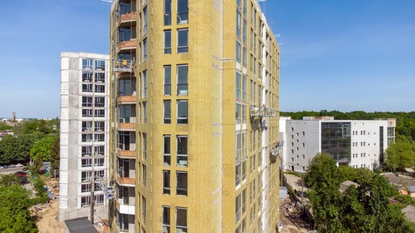 Construction site: Tall buildings under construction with yellow insulation, clear sky.
