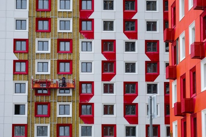 Building exterior with white facade, red window trim, construction worker on lift.