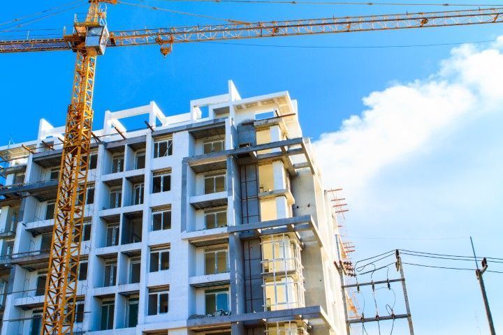 Construction of a multi-story building with a crane against a blue sky.