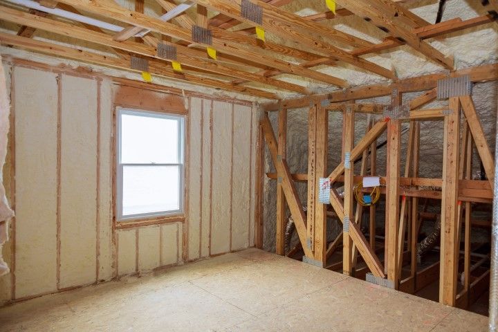 Interior room under construction, with spray foam insulation on walls and ceiling. Wooden beams are visible.