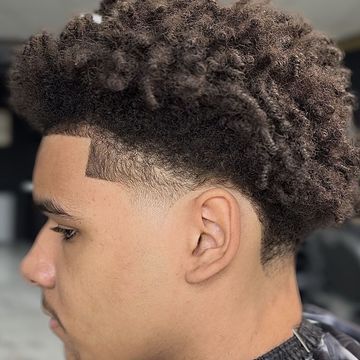 A young man with curly hair is getting his hair cut by a barber.
