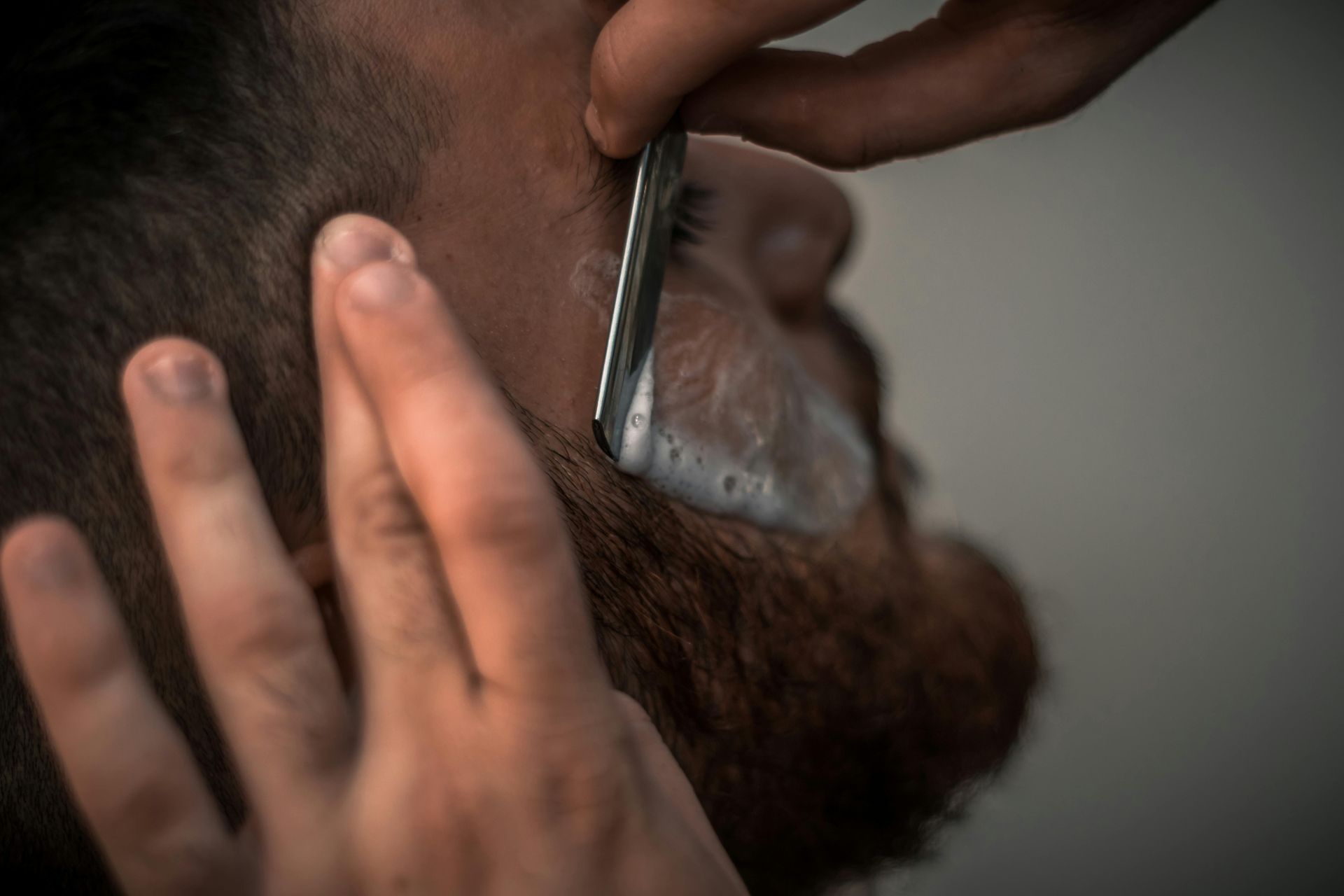 A man is getting his beard shaved by a barber with a razor.