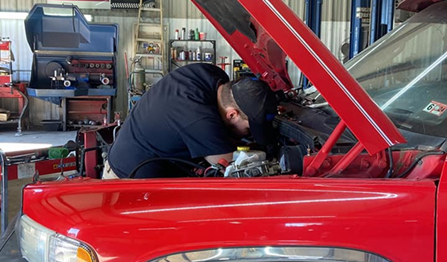 A person is working under the hood of a red truck | Gary's Automotive Again