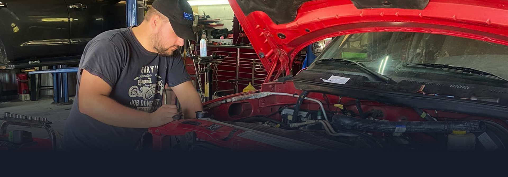 A person is working on the engine of a red car in a garage | Gary's Automotive Again