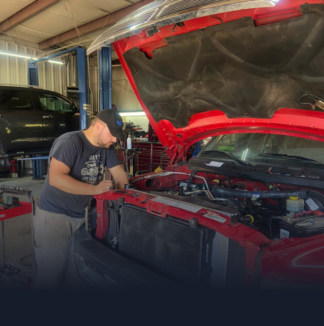 A person is working under the hood of a red car | Gary's Automotive Again