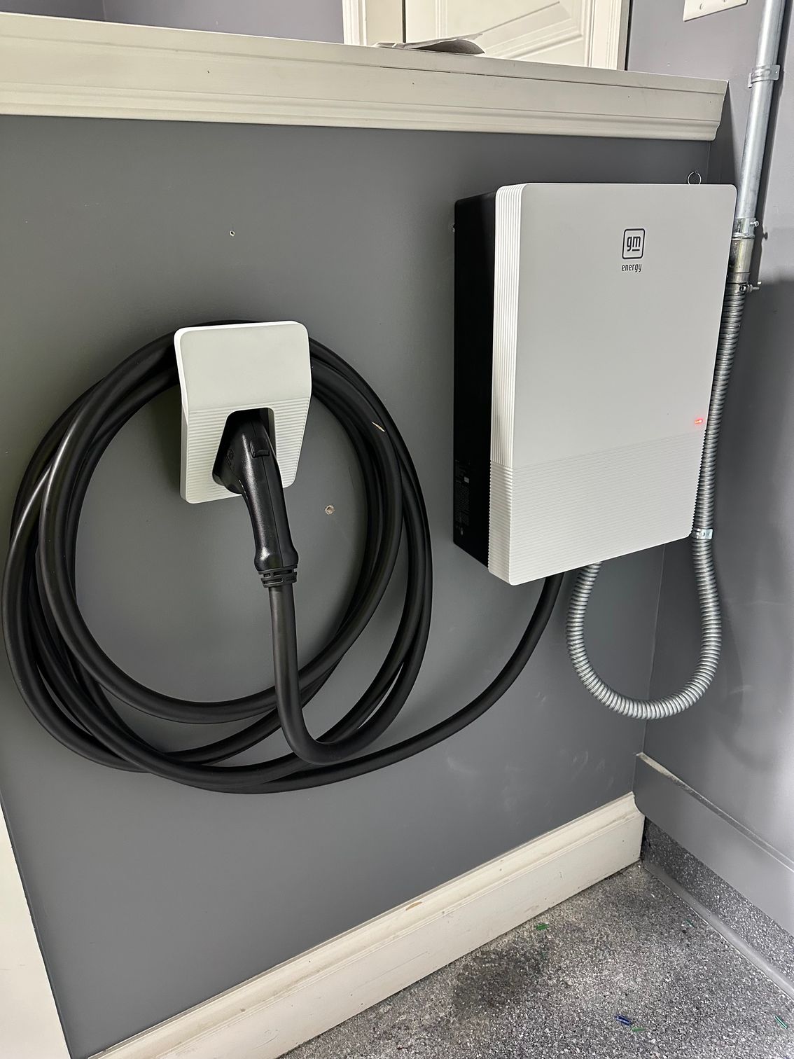 An electric vehicle charger mounted on a gray wall with its cover removed, exposing internal circuitry.