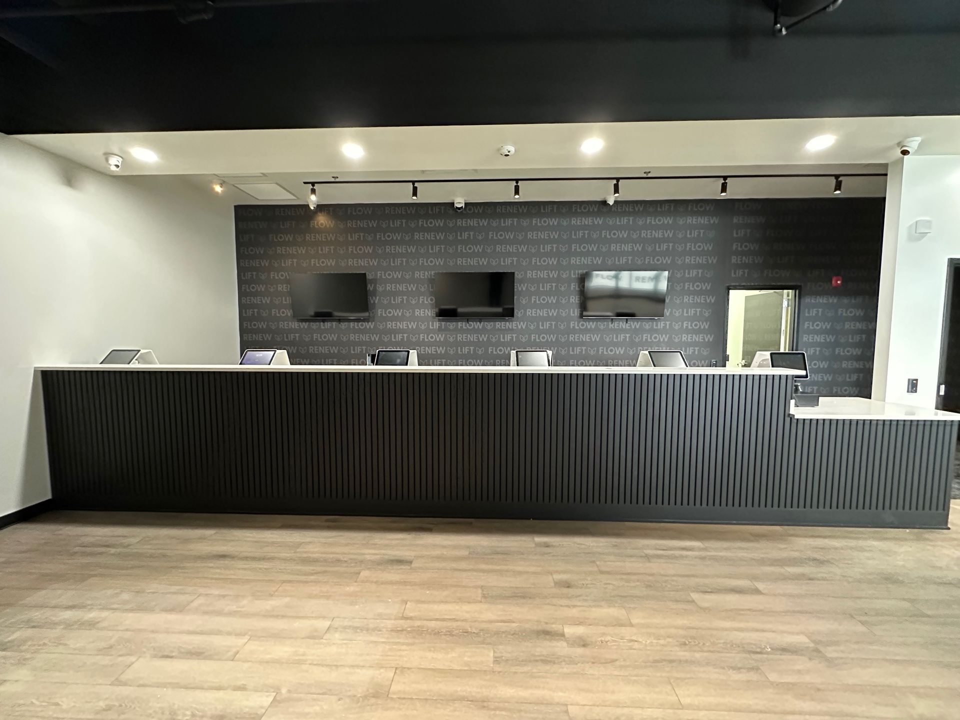 Reception desk in a modern retail space with three mounted screens against a textured wall.