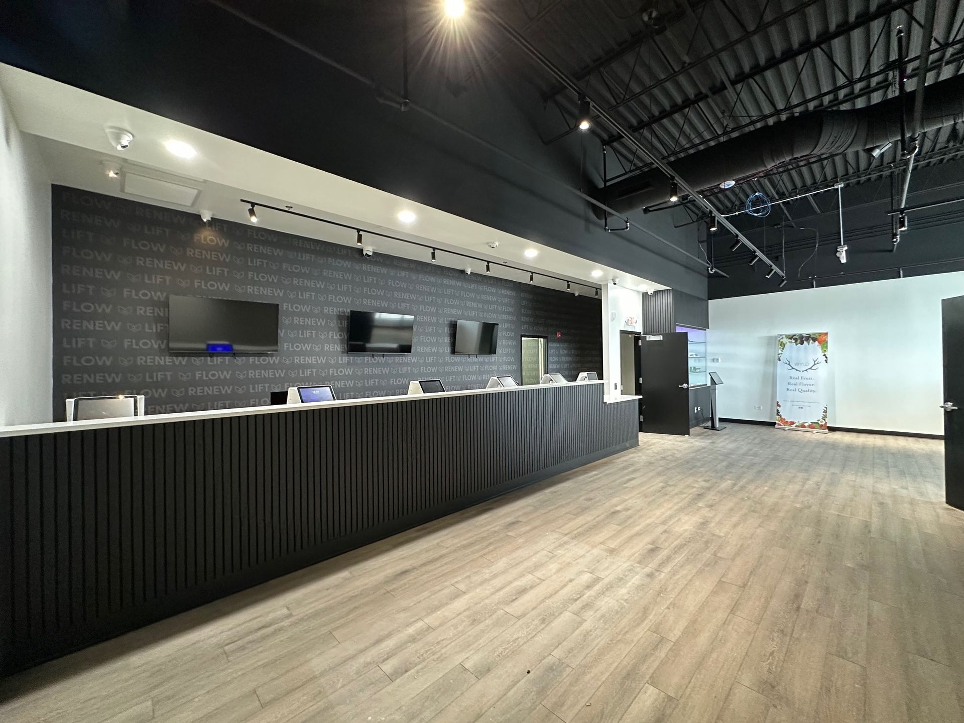 Interior of a modern retail space with a long counter, three screens, and black and light wood accents.