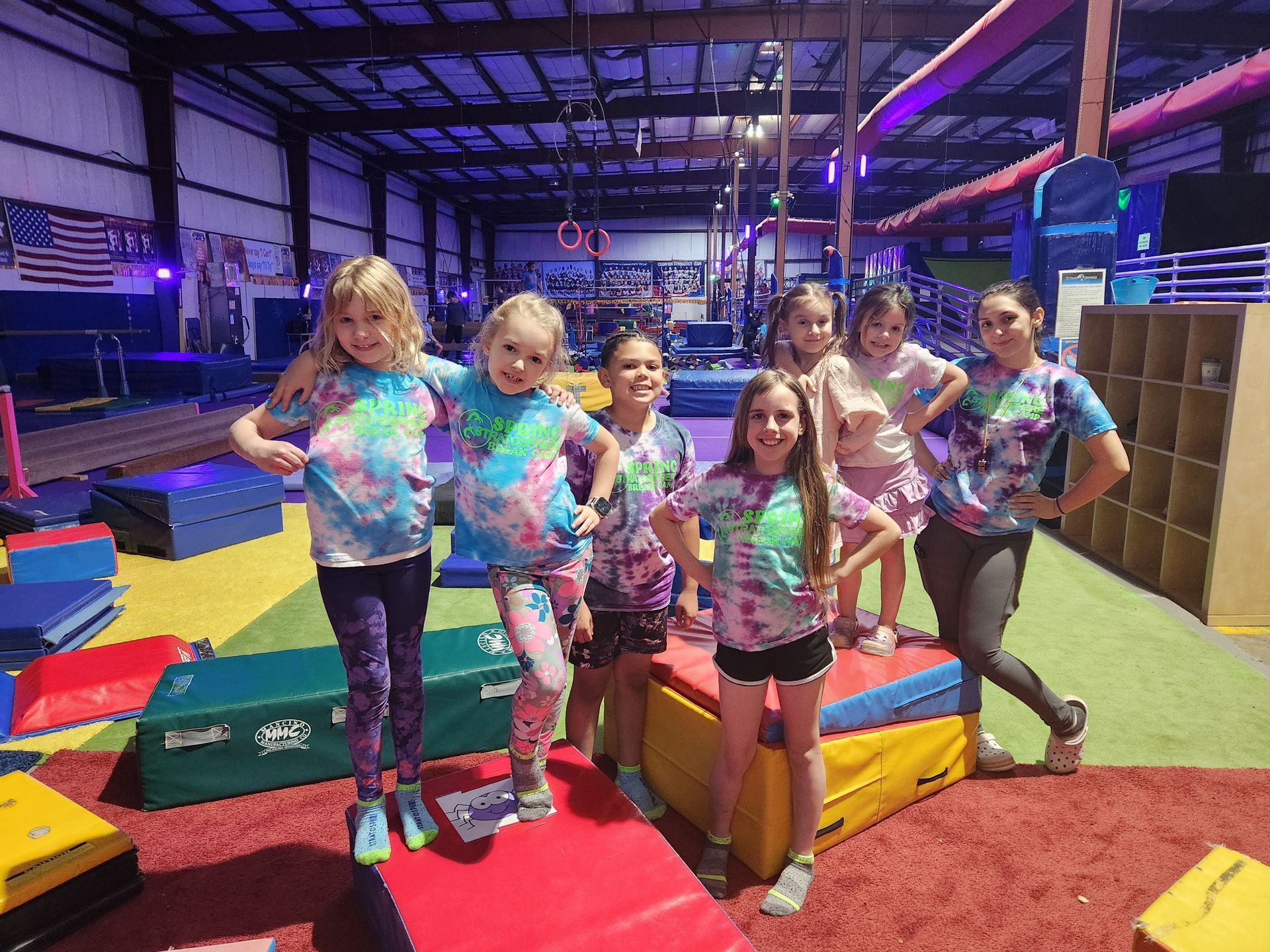 Group of children and an adult in tie-dye shirts pose in an indoor play gym.