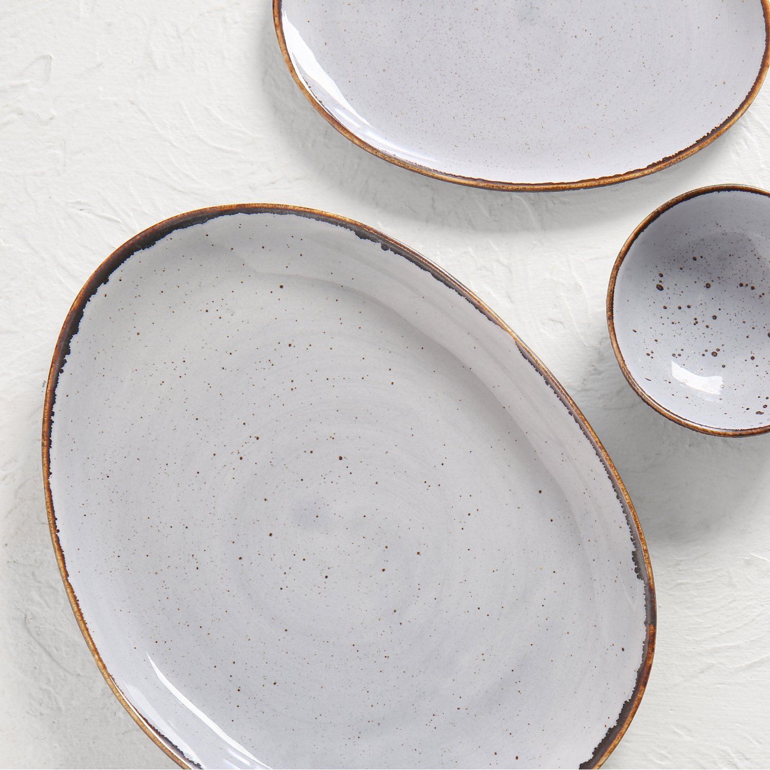 Oval white ceramic plate with a thin gold rim on a plain background