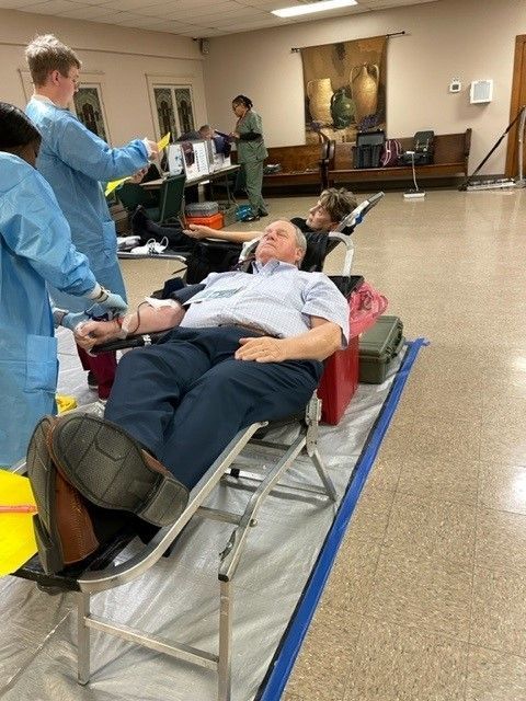Older man donating blood while a nurse assists him.