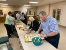 A group of people are standing around a long table eating food.