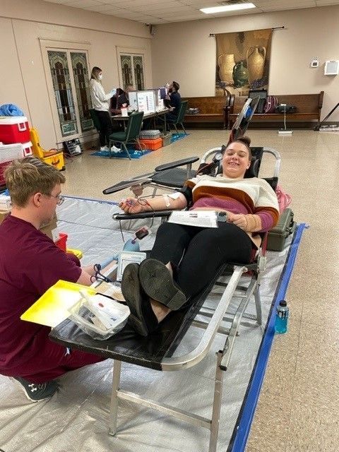 Person donating blood while smiling, with a nurse assisting.