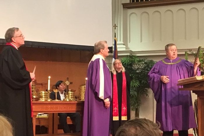 A group of men in purple robes are standing around a podium in a church.