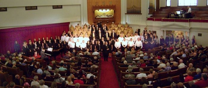 A large group of people are sitting in a church watching a choir perform.