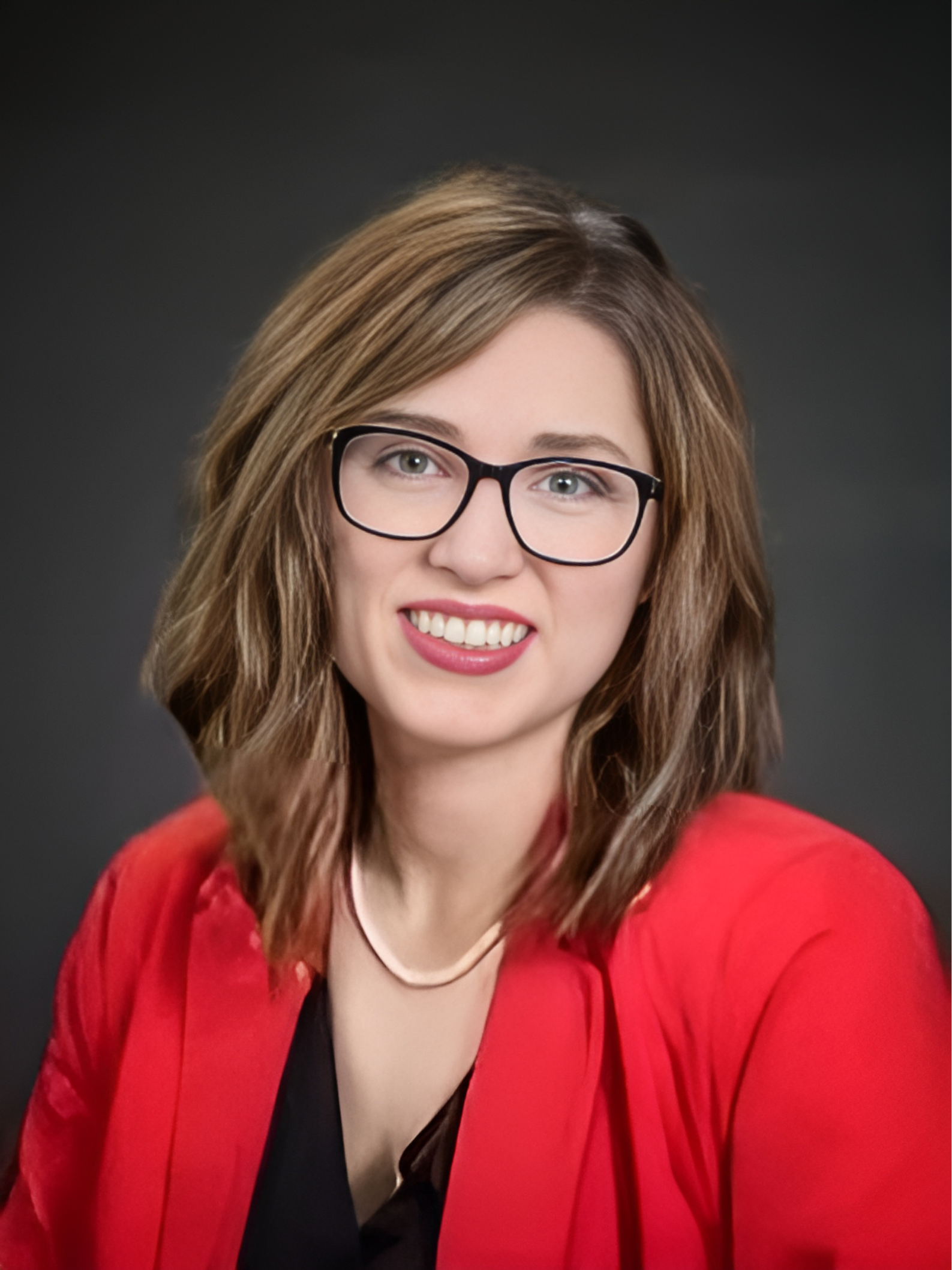 A woman wearing glasses and a red jacket is smiling for the camera.