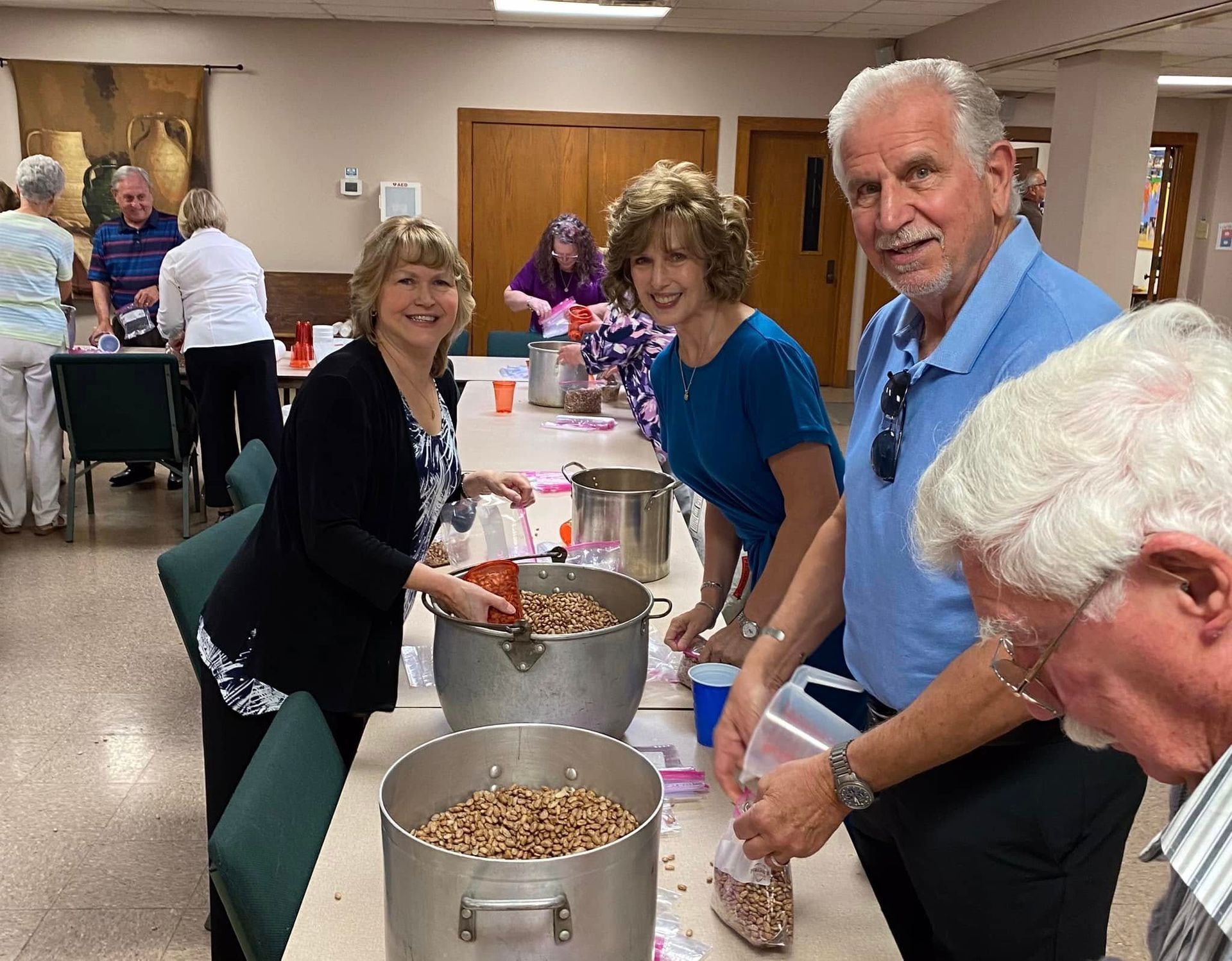 People filling bags from large pots on a table in a brightly lit room.