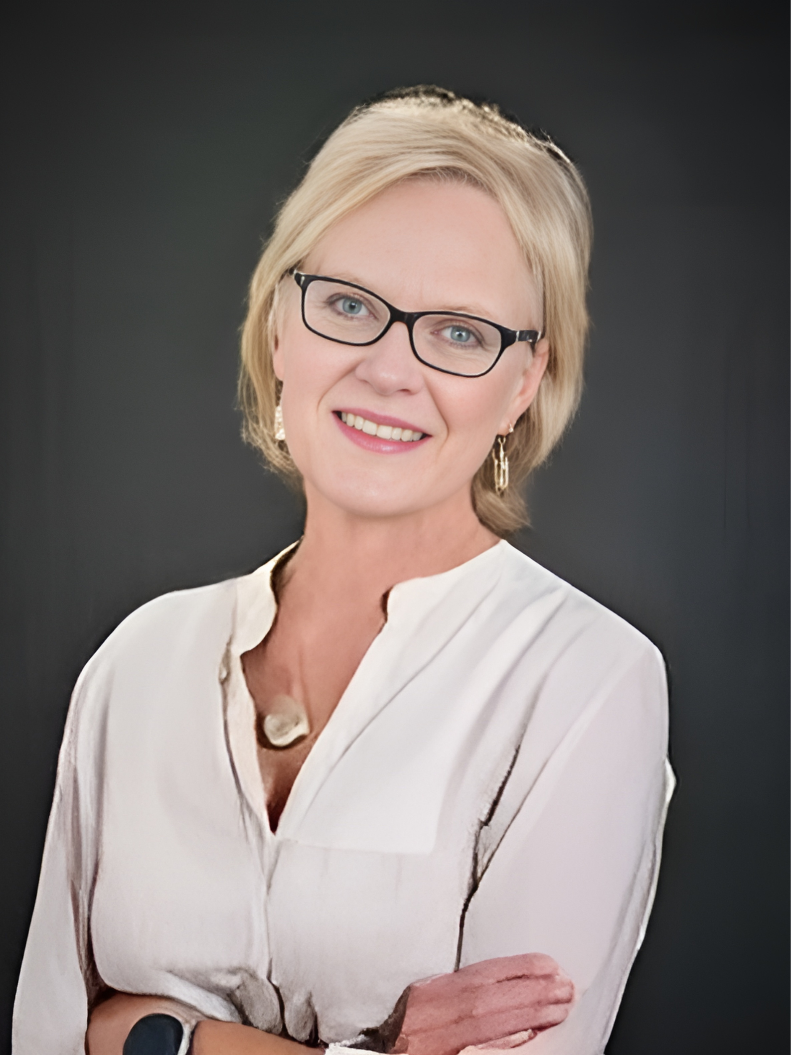 A woman wearing glasses and a white shirt is smiling with her arms crossed.