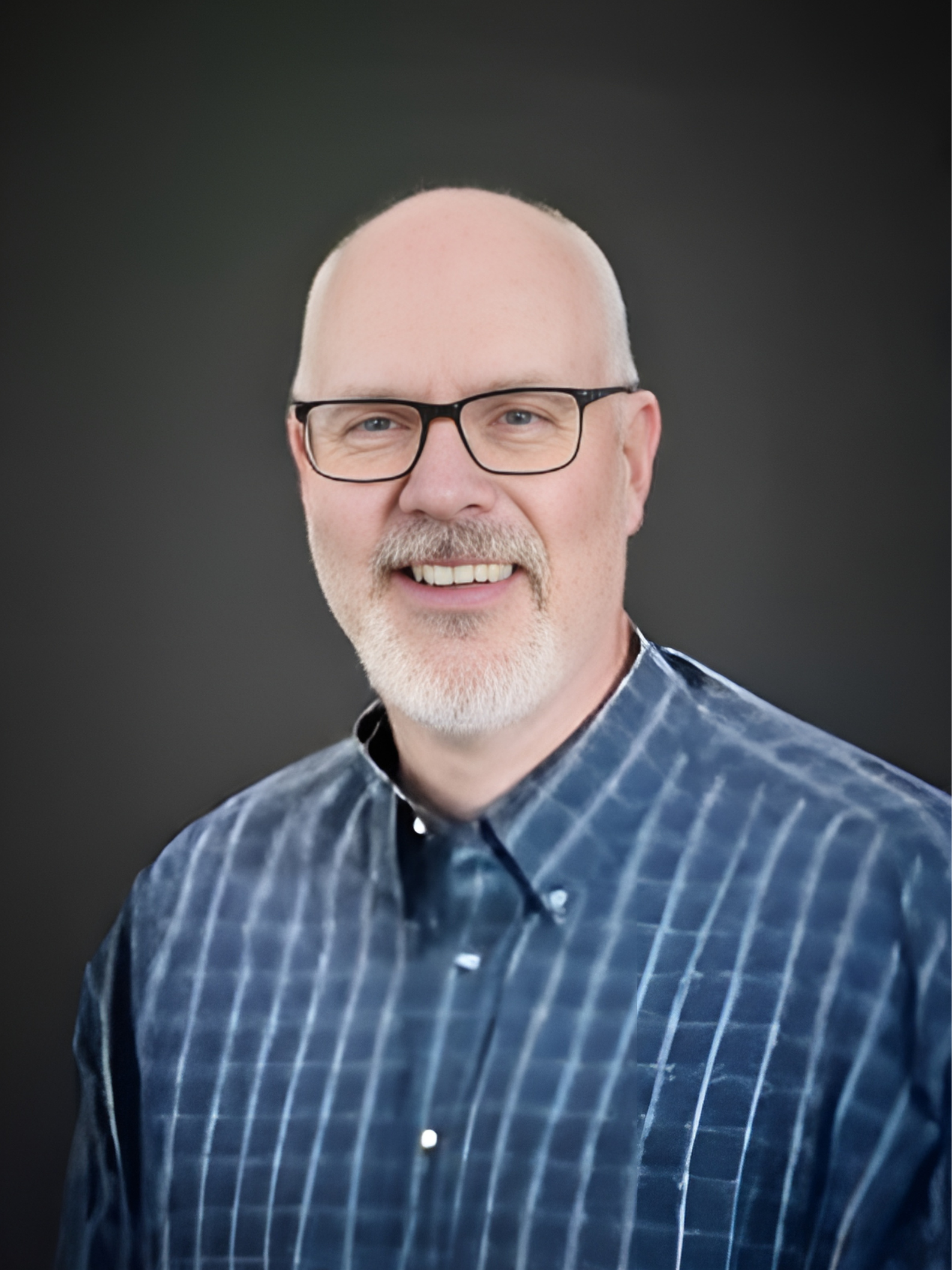 A man wearing glasses and a blue plaid shirt is smiling for the camera.