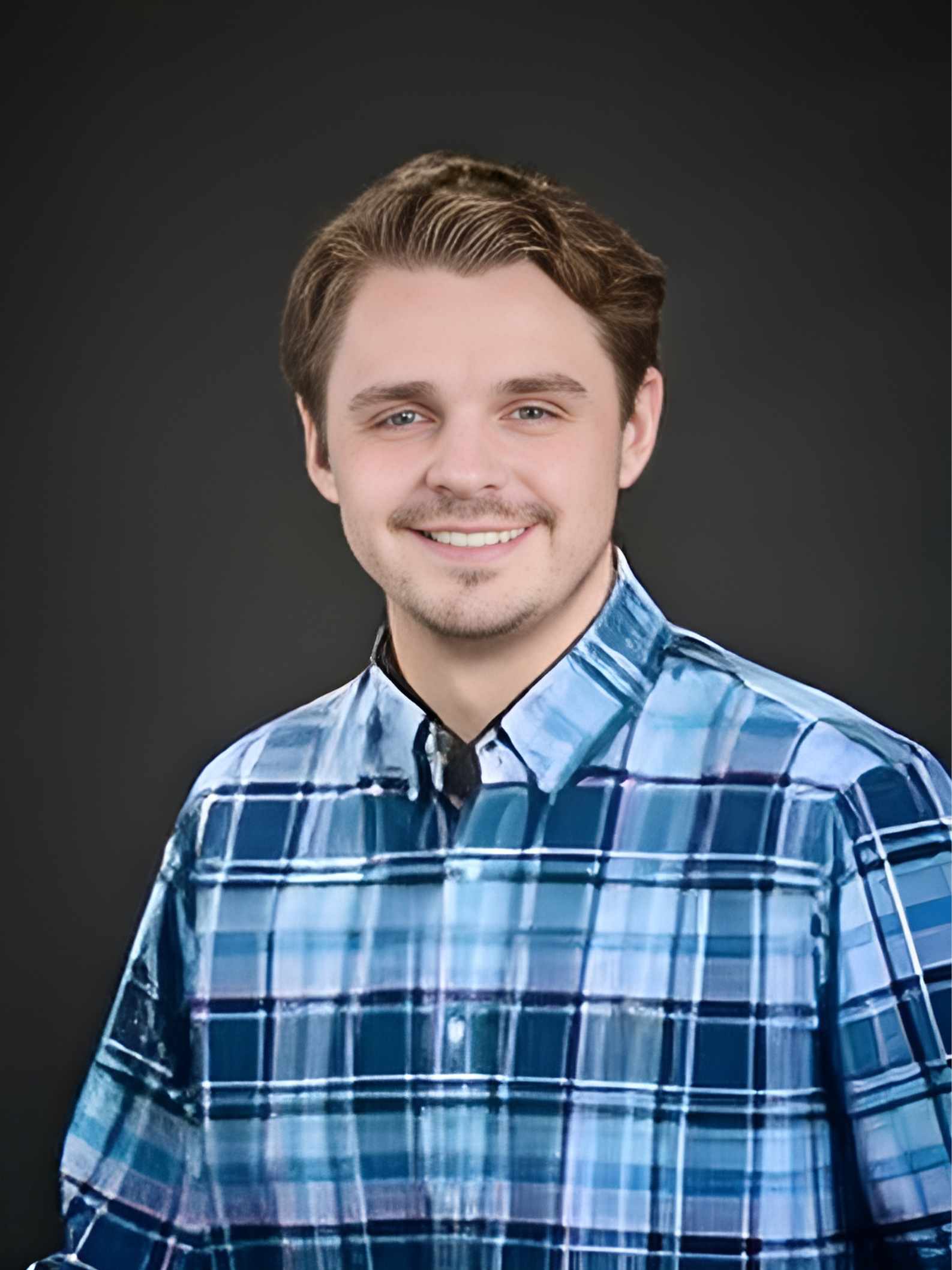 A young man in a blue plaid shirt is smiling for the camera.