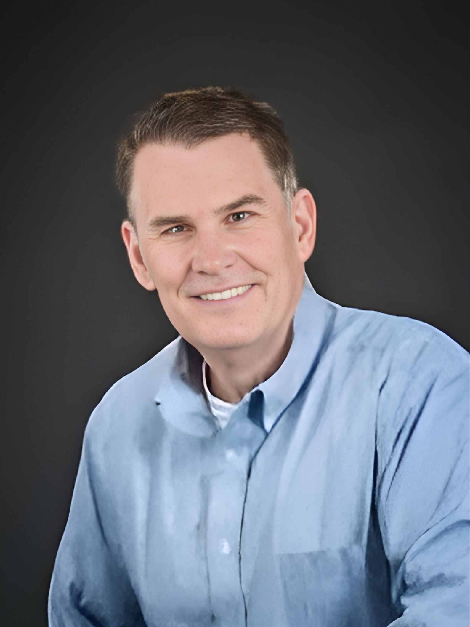 A man in a blue shirt is smiling for the camera.