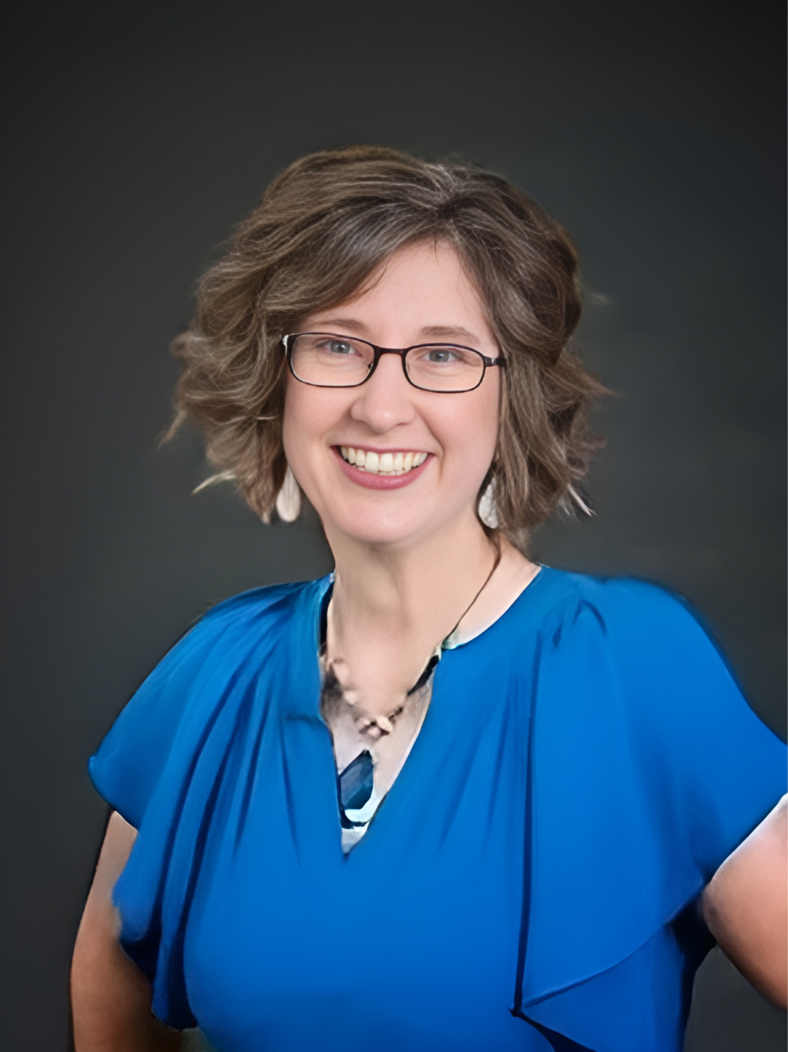 A woman wearing glasses and a blue shirt is smiling for the camera.