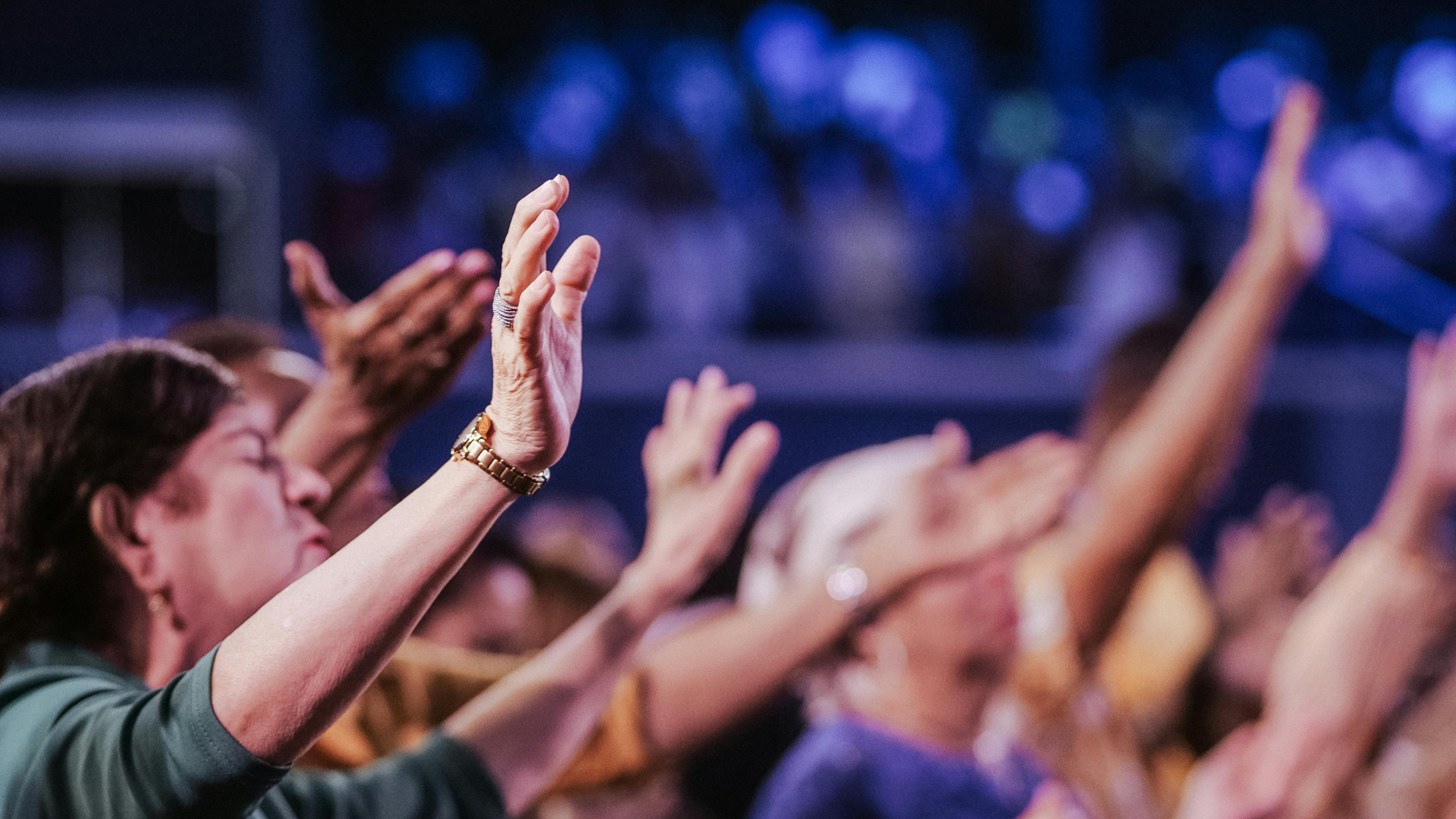 People with raised hands, possibly in worship, against a blurred blue background.