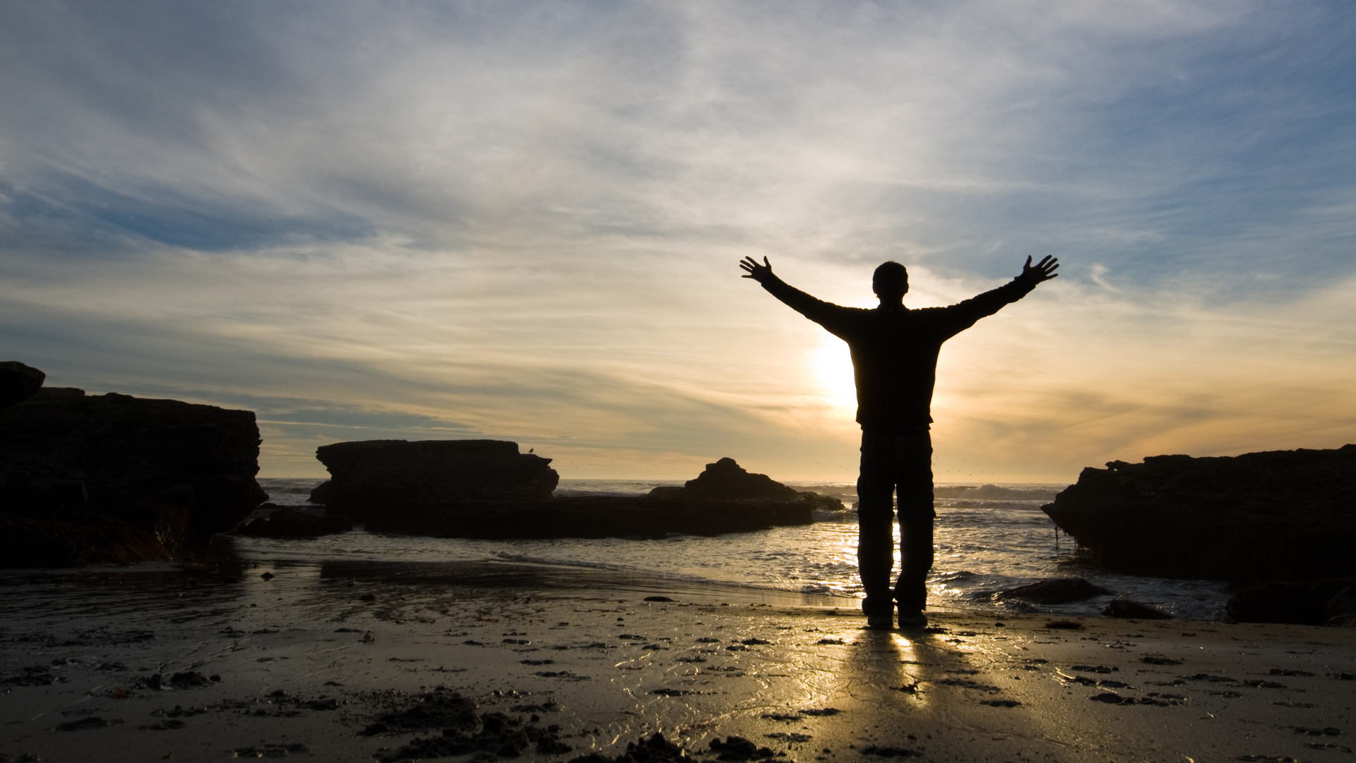 A man standing on a beach with his arms outstretched
