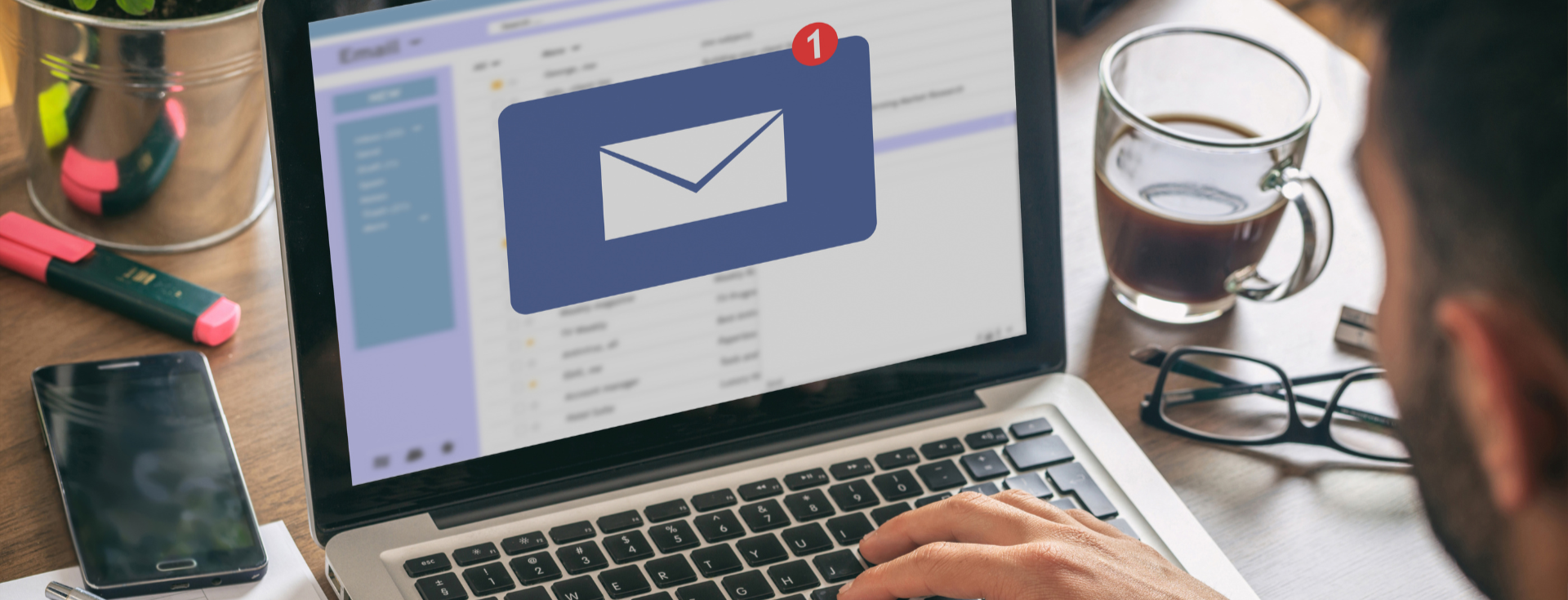 Person at a laptop checking email, with a cup of coffee and a phone on the desk.