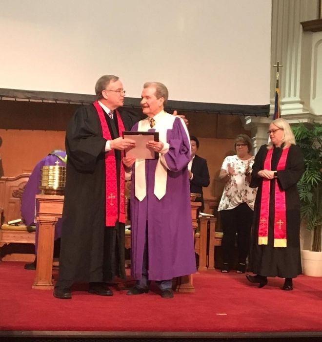 A man in a purple robe is being presented with a certificate