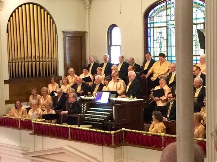 A choir singing in a church with a stained glass window in the background