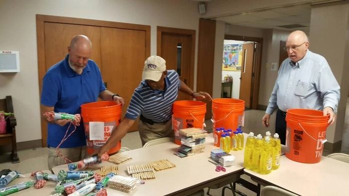 Three men are standing around a table holding orange buckets