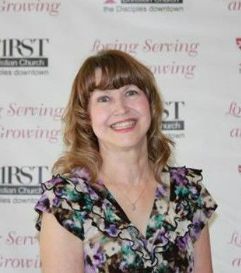 A woman is smiling in front of a sign that says first