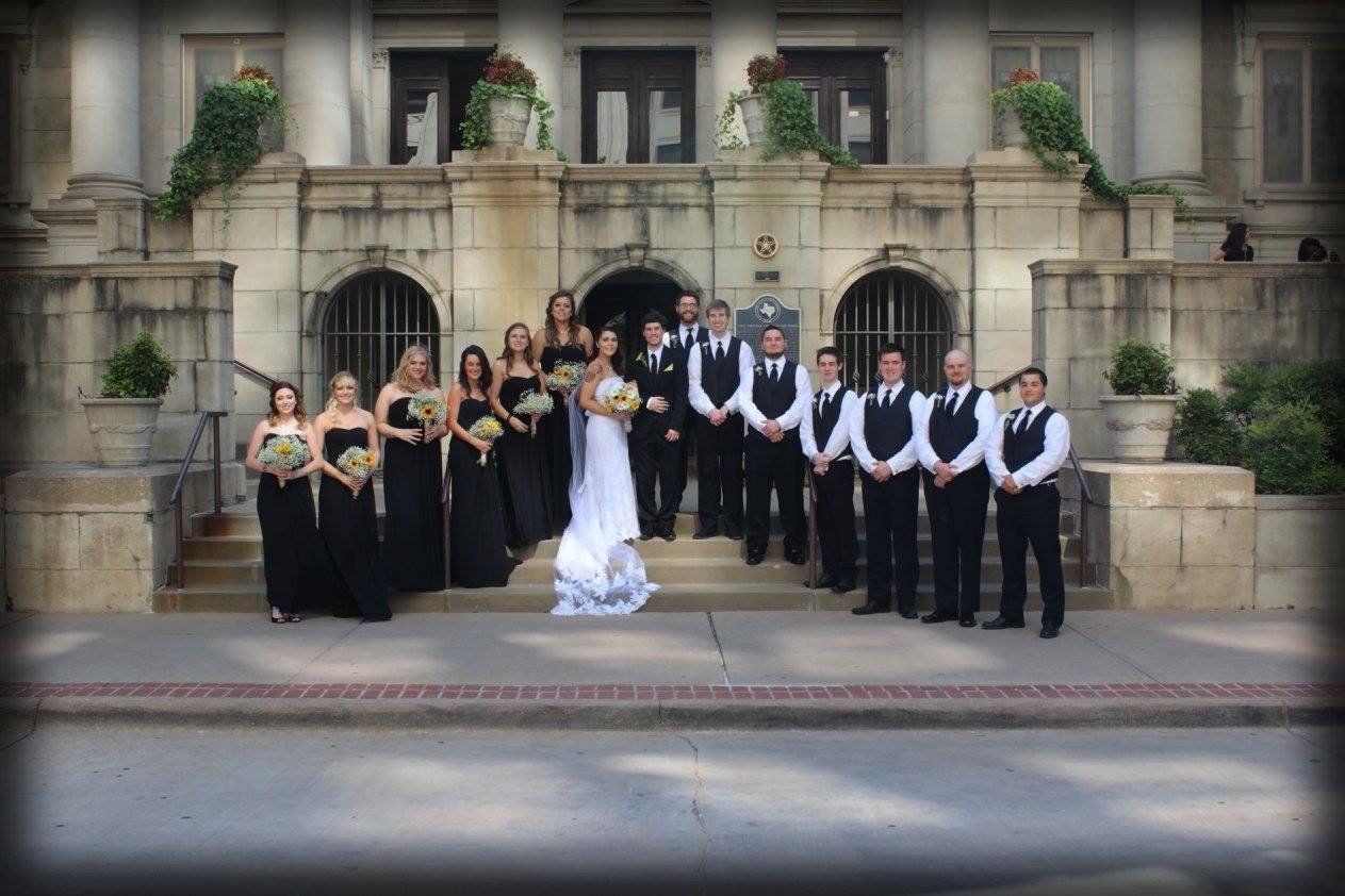 A bride and groom pose with their wedding party in front of a building.