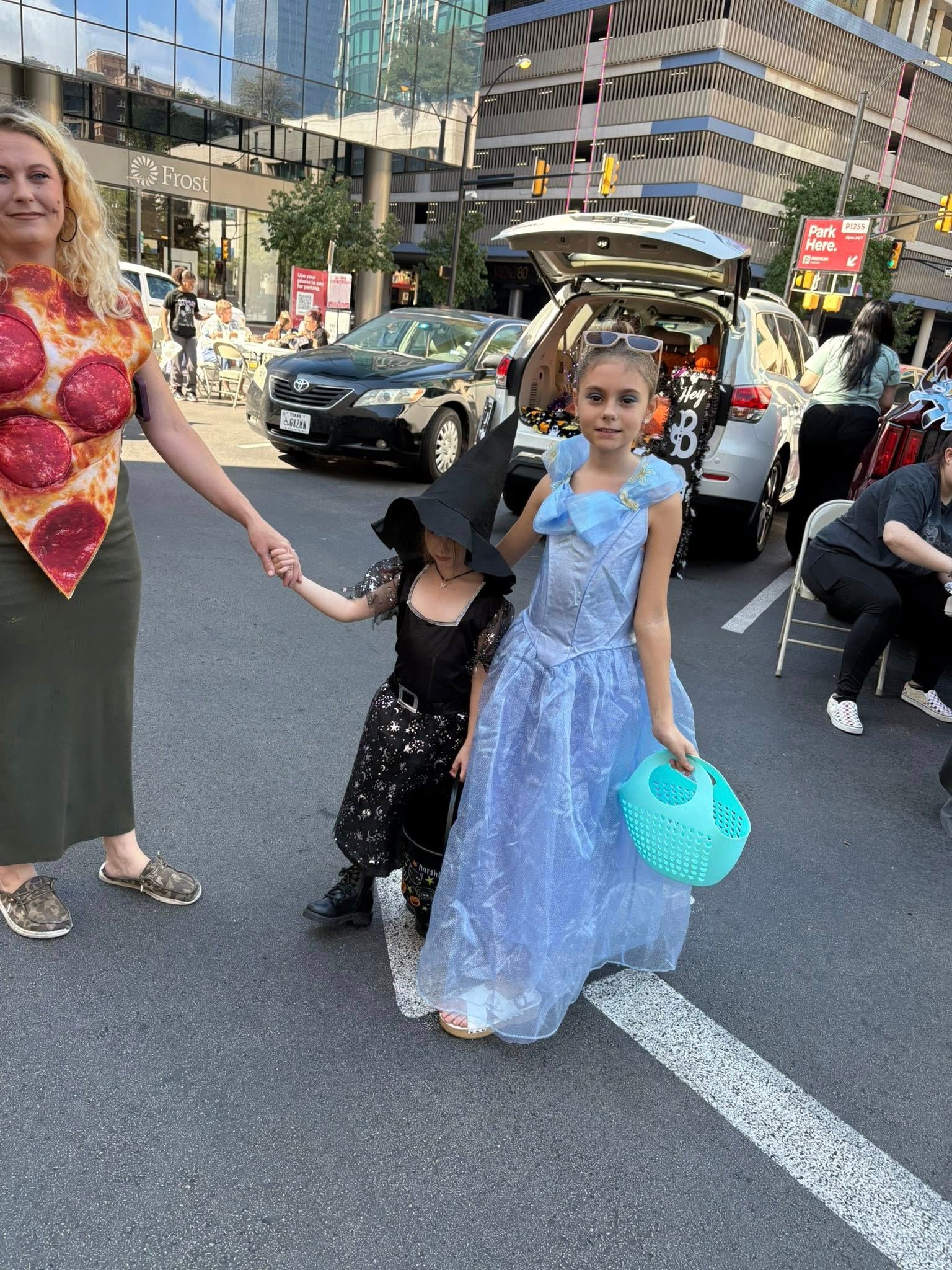 Woman in pizza costume with two trick-or-treaters: witch and princess, at a trunk-or-treat event.