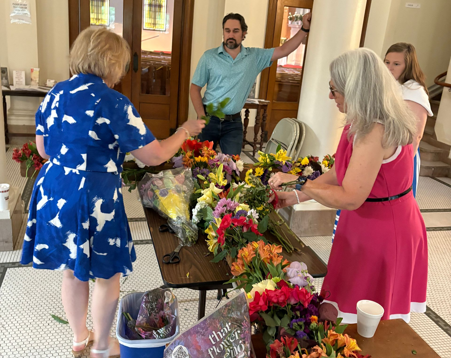 People arranging colorful flowers on a table inside a building.