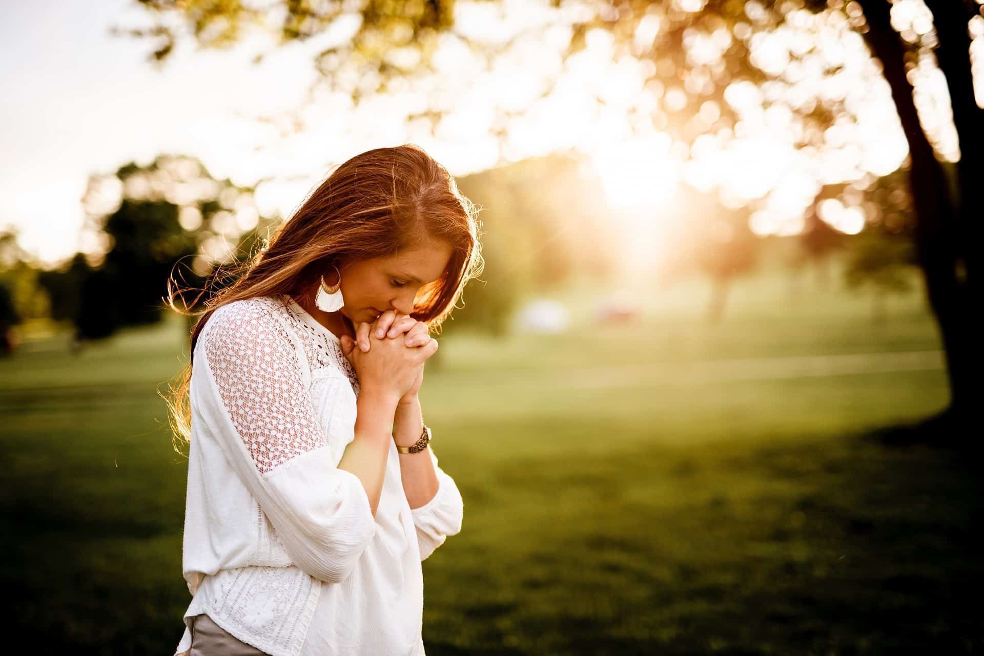 A woman is praying in a park with her hands folded.