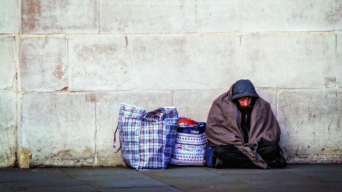 Homeless person sitting on the ground with bags next to them.