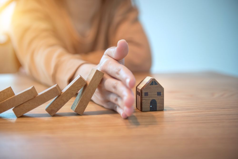 Hand Stopping a Row of Falling Dominoes Before They Hit a Miniature House — Precision Financial & Tax In Ross Creek, VIC