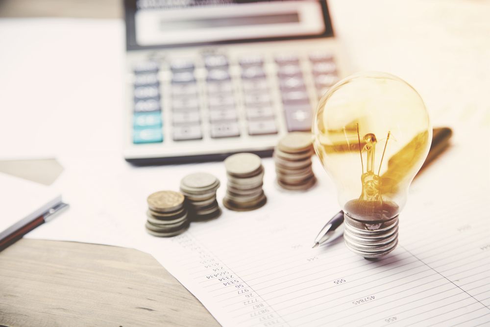 Stacks of Coins Next to a Lit Lightbulb and Calculator — Precision Financial & Tax In Ross Creek, VIC
